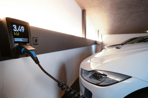 Electric vehicle connected to wall-mounted charging unit displaying energy output, illustrating battery system usage, electrical infrastructure, and safe energy management in EV operations.