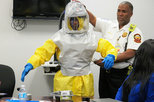 A compliance officer in protective equipment standing with a facility worker reviewing hazardous materials procedures, illustrating the training and documentation requirements for hazardous materials storage compliance under DOT and OSHA regulations.