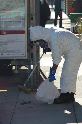 A responder in white protective coveralls addresses a hazardous materials incident on a public sidewalk, illustrating the on-scene response that follows a hazmat release.